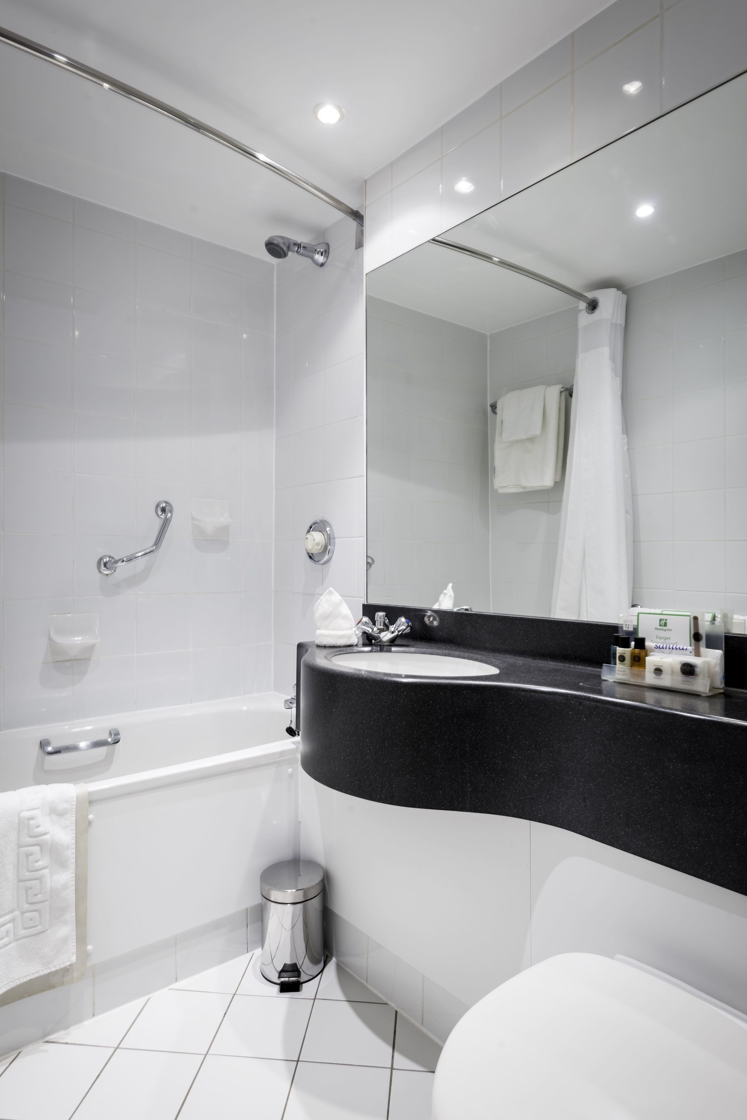 Un baño moderno con lavamanos de superficie negra, inodoro blanco, ducha con puerta de vidrio y espejo sobre el lavamanos.