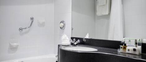 Un baño moderno con lavamanos de superficie negra, inodoro blanco, ducha con puerta de vidrio y espejo sobre el lavamanos.