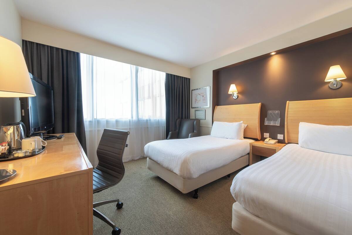 Une chambre d’hôtel avec deux lits, un bureau avec une machine à café, une télévision et une grande fenêtre avec des rideaux.