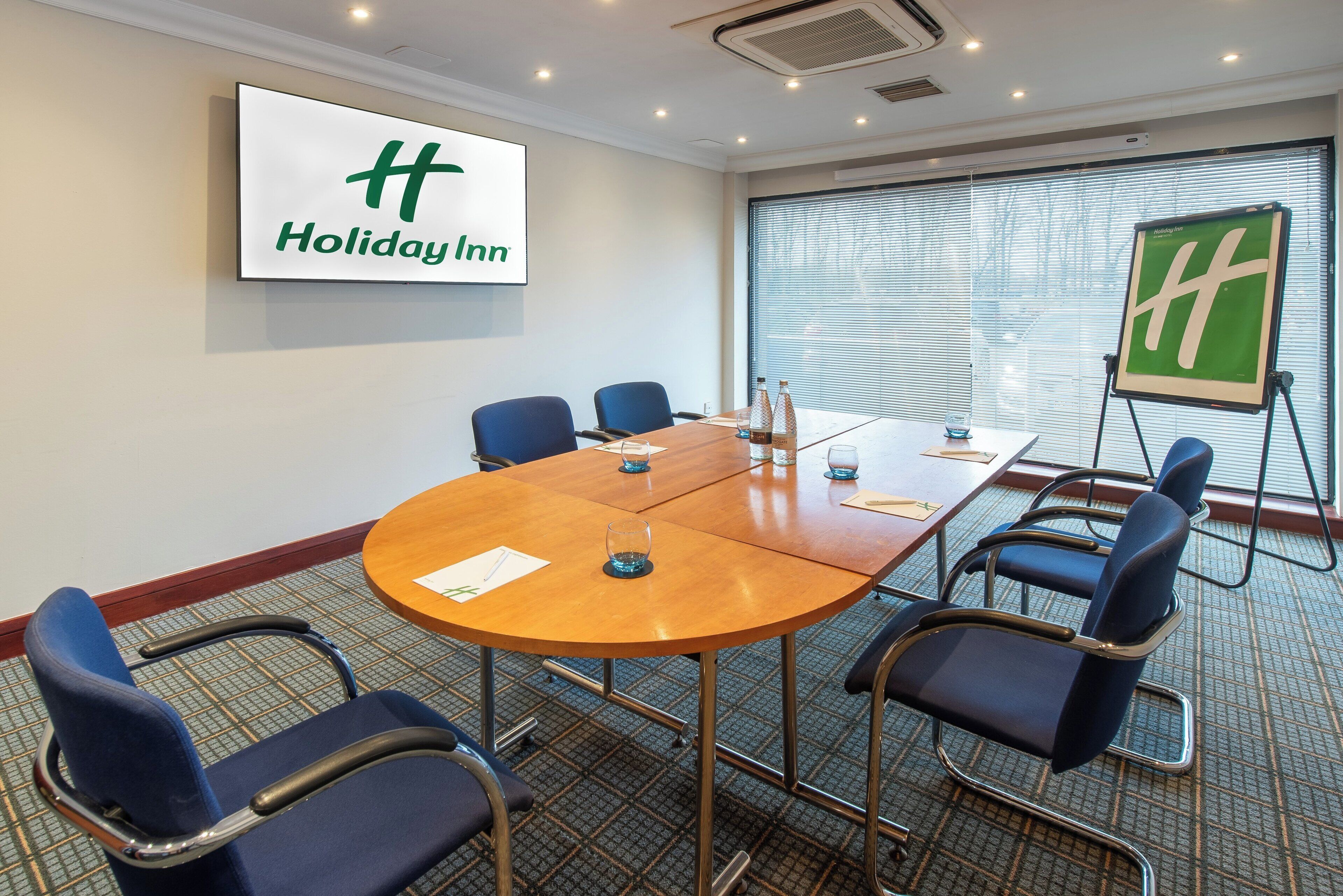 A conference room with a large table, blue chairs, a Holiday Inn sign, and a flip chart.