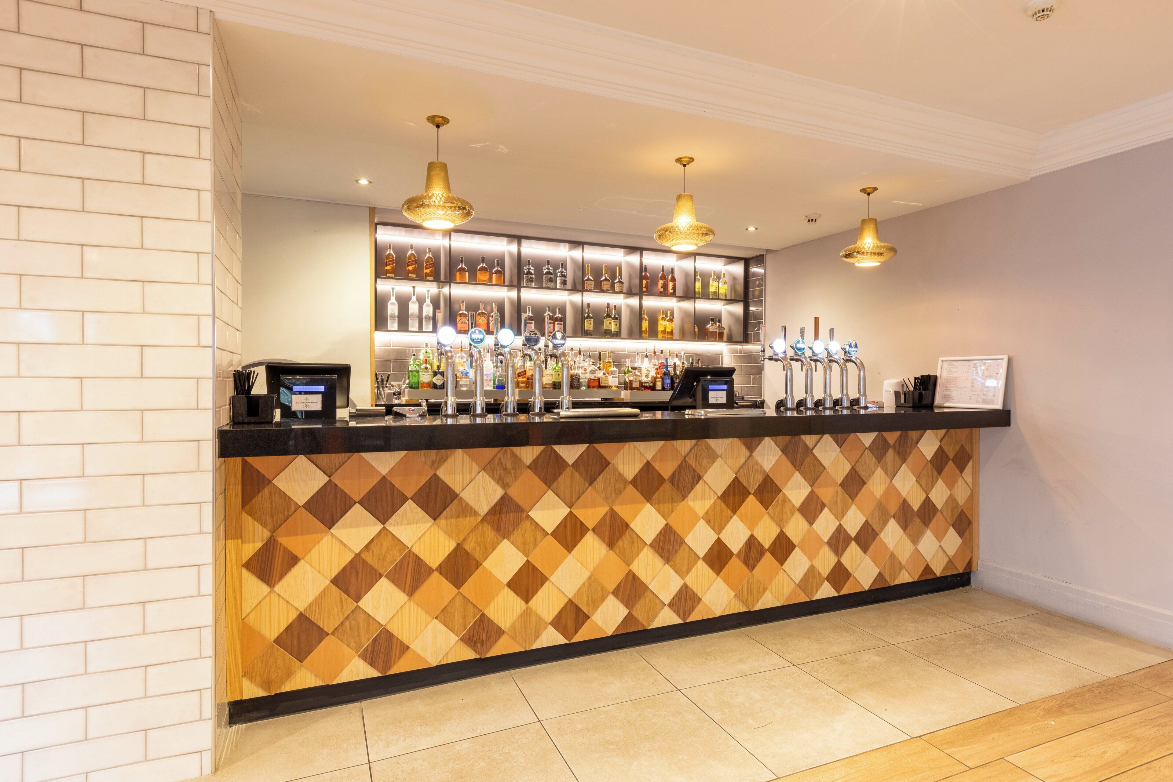 A bar area with a patterned wall, multiple liquor dispensers, and pendant lighting.