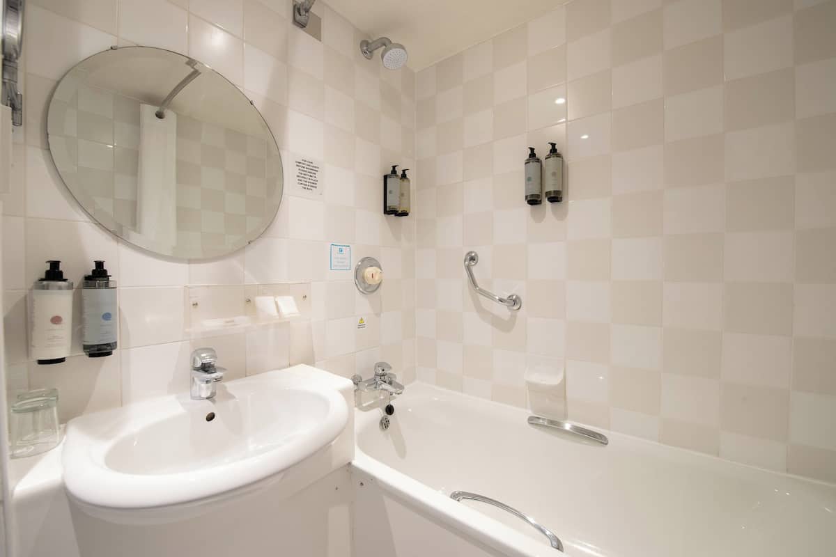 A bathroom with a white sink, a bathtub, a round mirror, and two wall-mounted soap dispensers.