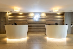 A reception area with two reception desks, a wooden wall with a hashtag symbol, and a ceiling light fixture. - Holiday Inn Glasgow Airport by IHG (Paisley)