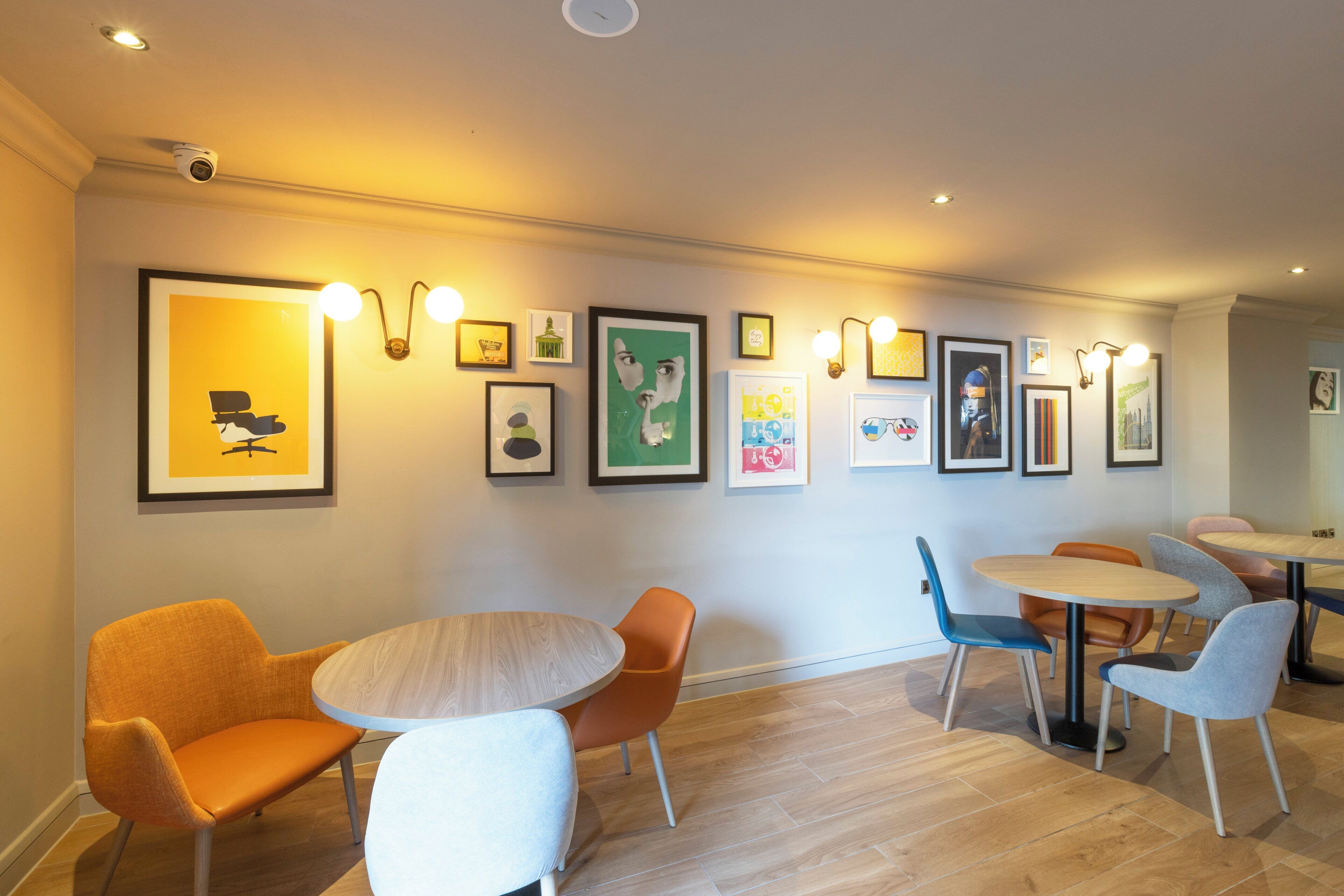 Un intérieur moderne avec un espace repas comprenant des tables et des chaises rondes, des œuvres d’art encadrées accrochées aux murs et une caméra de surveillance fixée au plafond.
