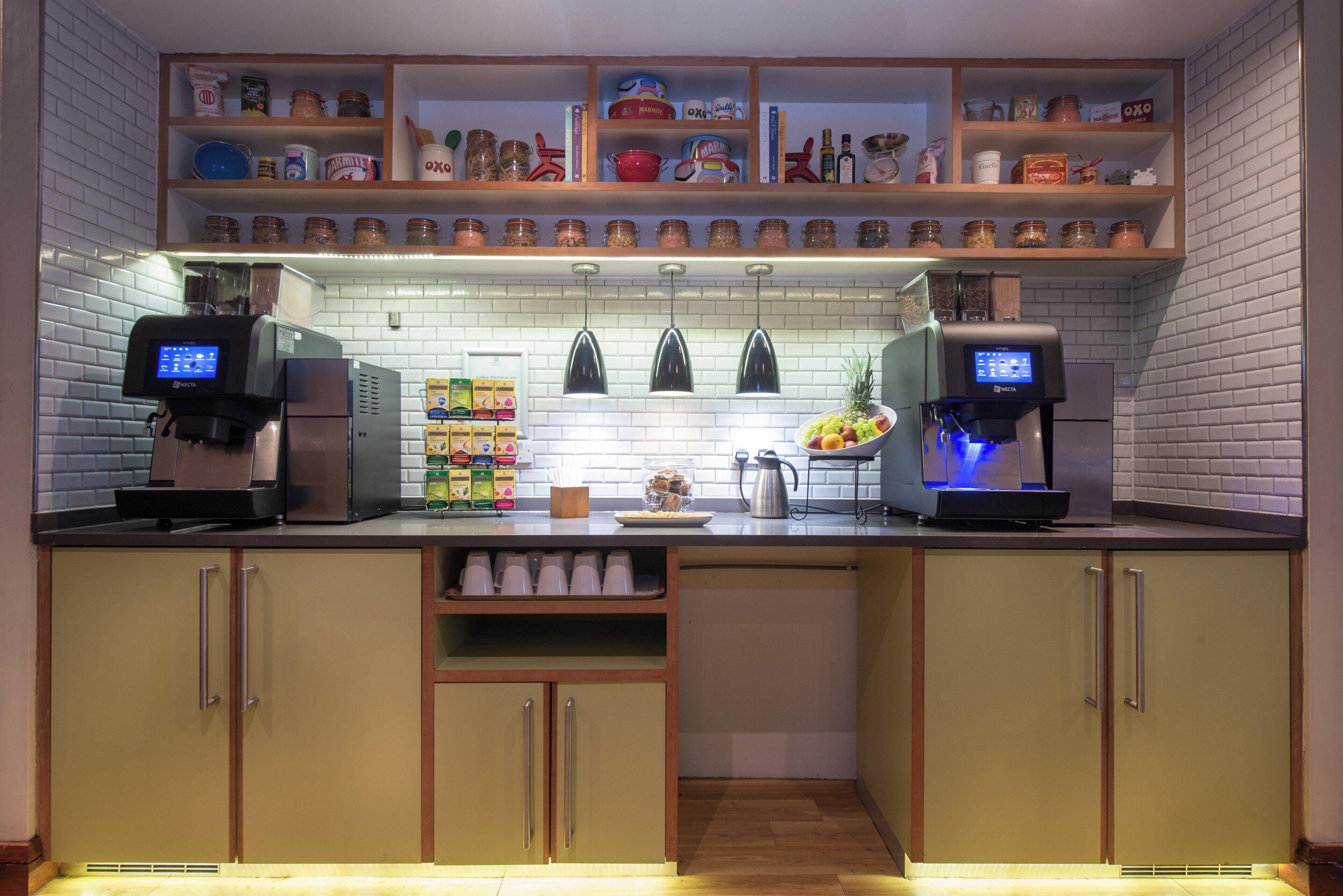 A kitchen with two coffee machines, a fruit bowl, and shelves with jars and kitchen items.