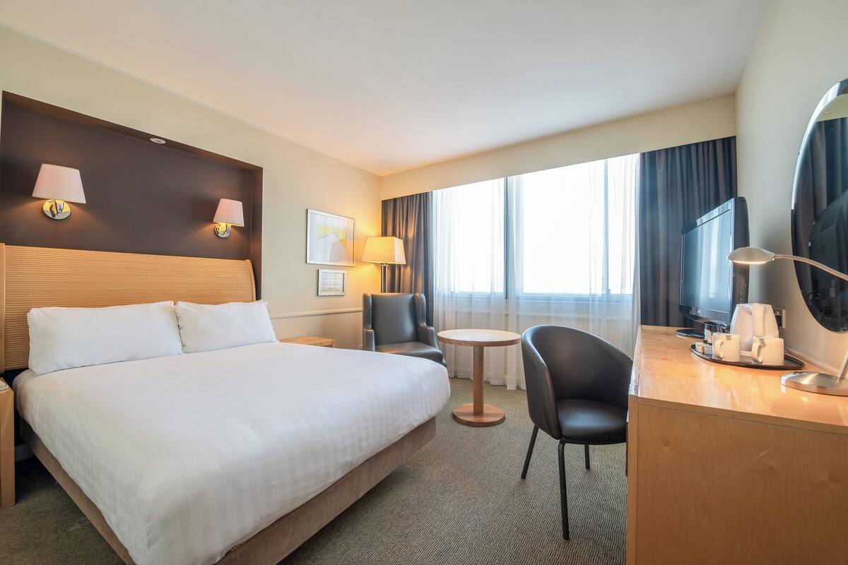 Une chambre d’hôtel avec un grand lit, un bureau avec une lampe, une chaise, une petite table ronde et un téléviseur.