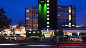 A Holiday Inn hotel with multiple floors, a parking lot with several cars, and a 'Meetings & Events' sign.