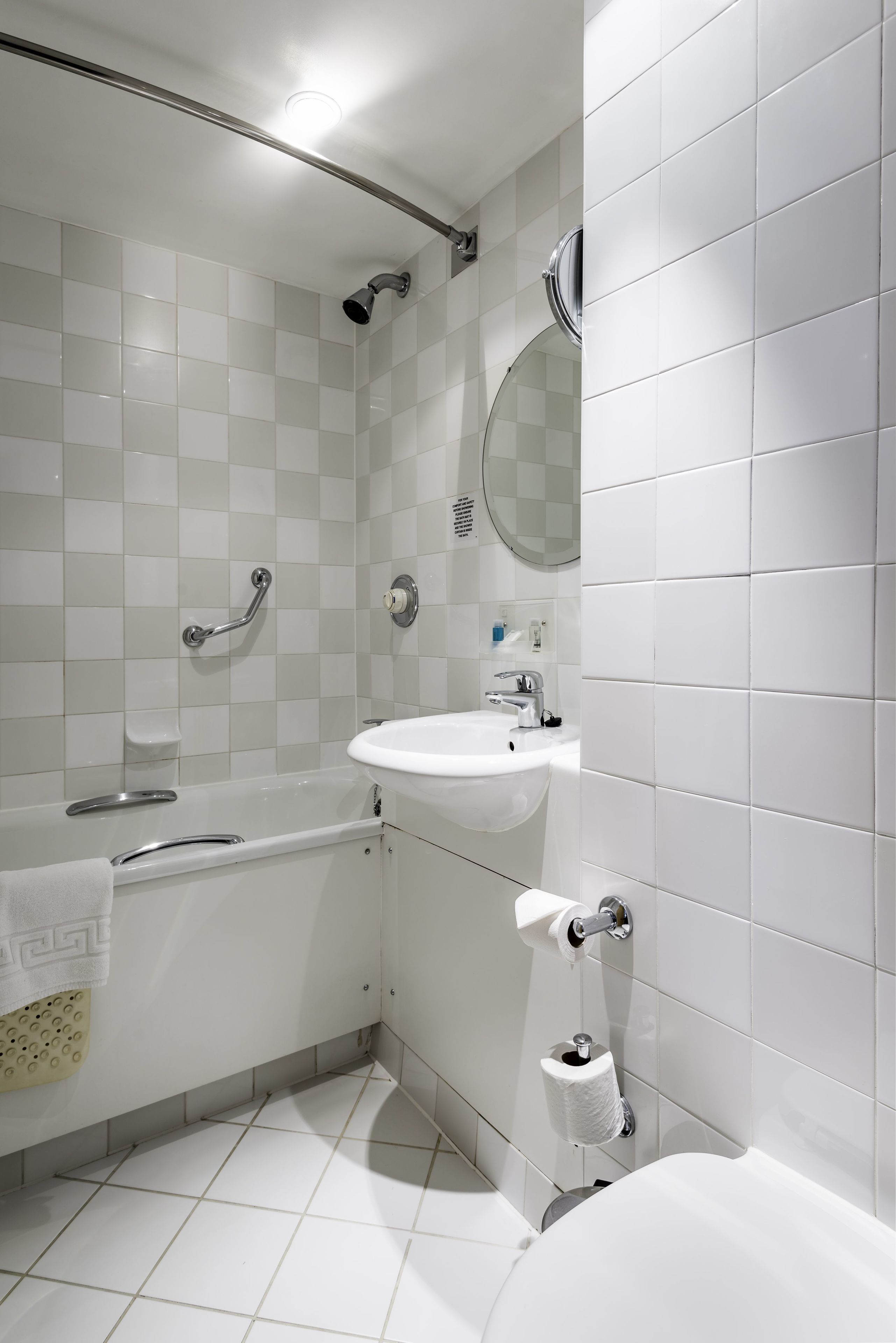 A modern bathroom with white tiles, a bathtub, a sink, and a shower.