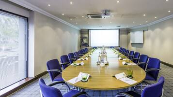 A conference room with a long table, blue chairs, and a projector screen.
