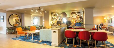 A modern hotel lobby with a central bar area, seating arrangements, and a decorative hexagonal wall design.