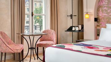 A hotel room with a bed, two patterned chairs, a small table, a nightstand, and a window with curtains.