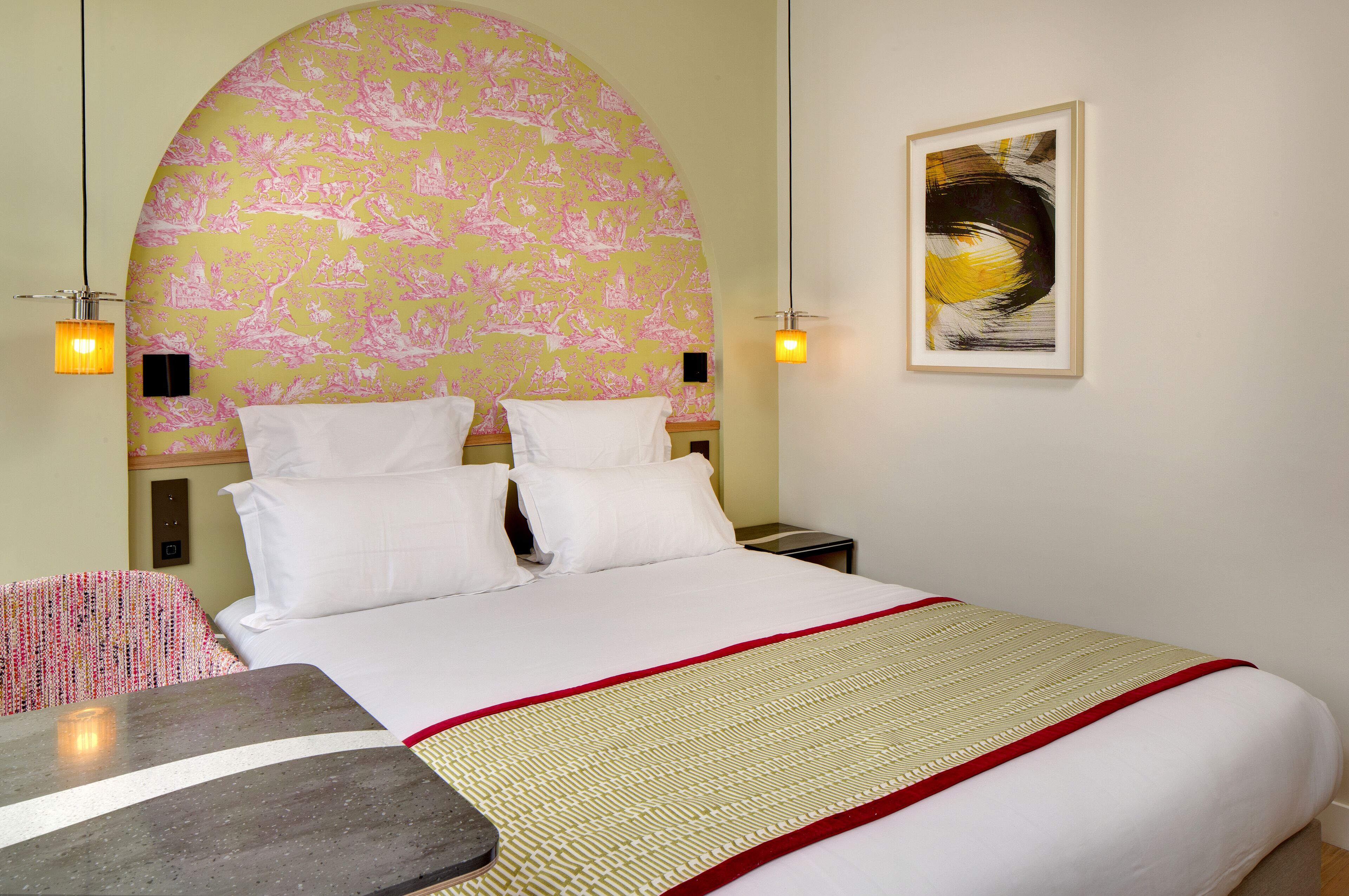Une chambre d’hôtel avec un grand lit, une arche décorative au mur, un tableau encadré et une petite table.