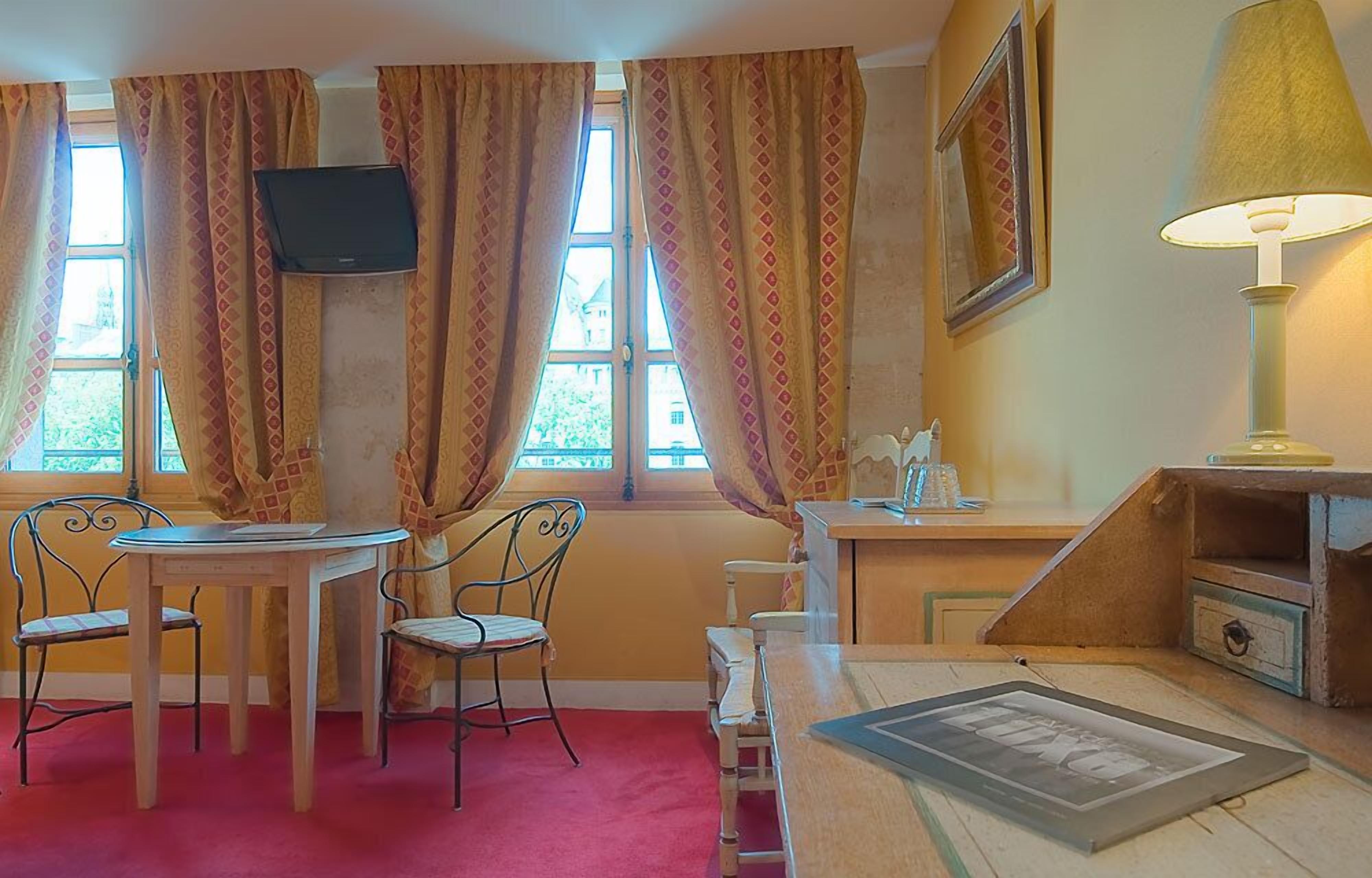 Ein Zimmer mit Esstisch und Stühlen, einem an der Wand montierten Fernseher, einer Lampe und einem Fenster mit Vorhängen.