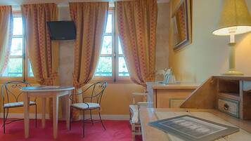Ein Zimmer mit Esstisch und Stühlen, einem an der Wand montierten Fernseher, einer Lampe und einem Fenster mit Vorhängen.