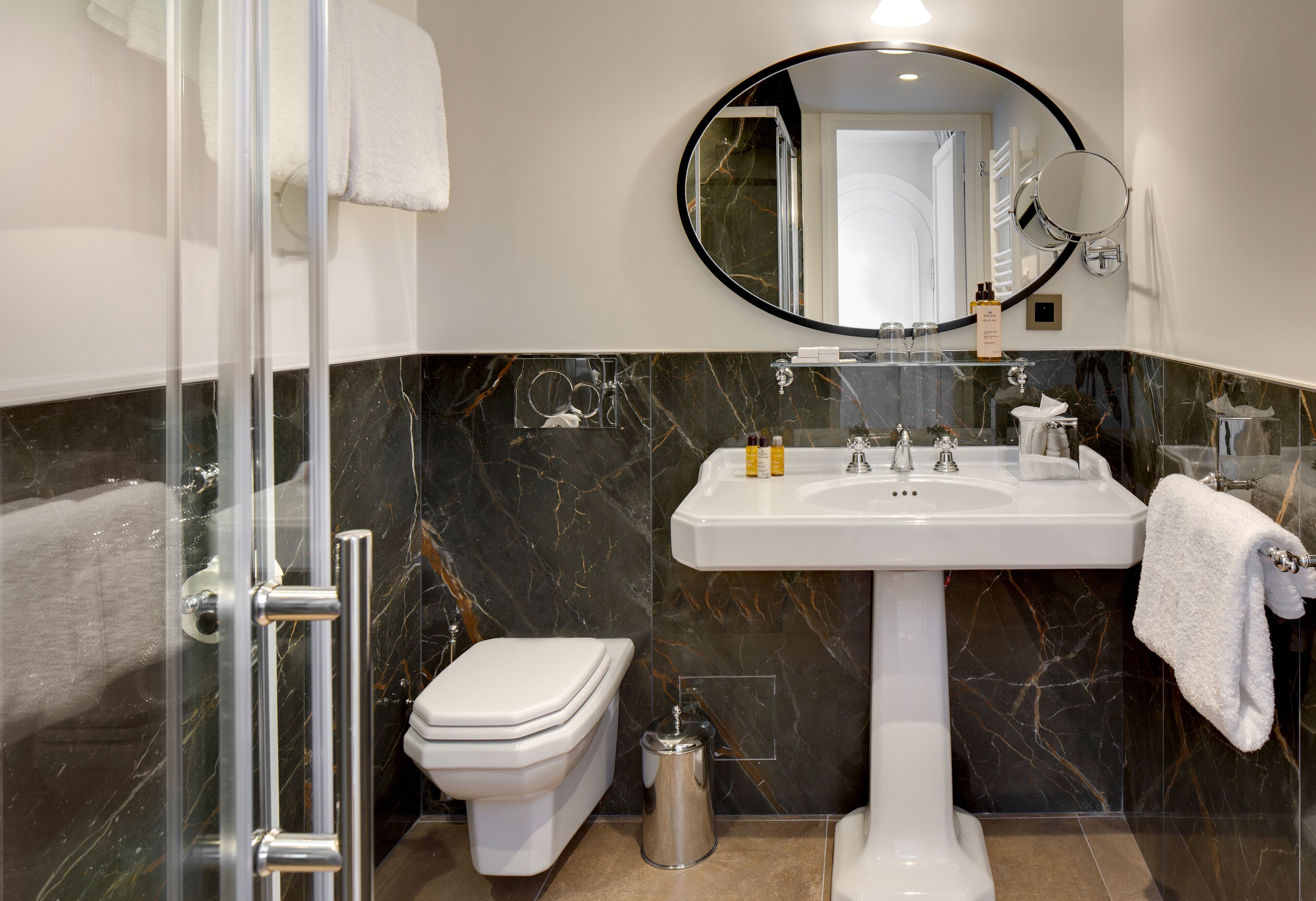 Une salle de bain moderne avec une douche à parois de verre, des toilettes blanches, un lavabo sur colonne et un grand miroir.