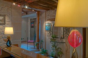 A room with stone walls, a wooden ceiling, a chair, and a table with a lamp.
