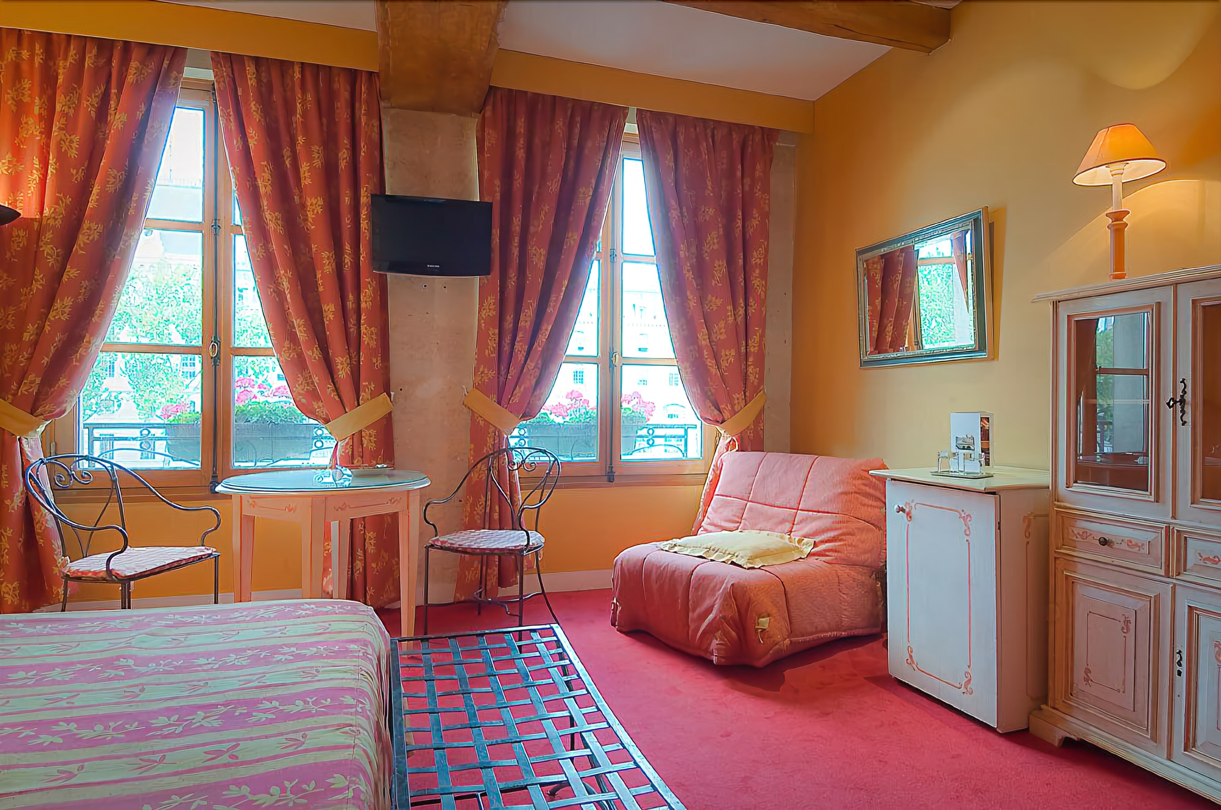 Una habitación con dos camas, una mesita, una silla, un armario y una ventana con cortinas.