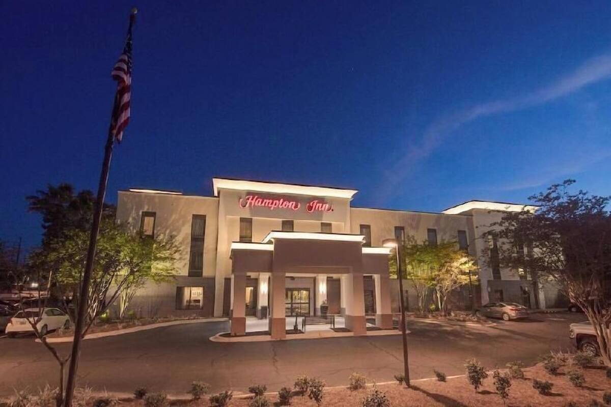 A hotel with a sign reading 'Hampton Inn.' It features a modern architectural style with a flat roof and a covered entrance.