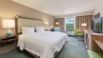Habitación de hotel con una cama grande, un escritorio con televisor, una silla y una ventana con cortinas.