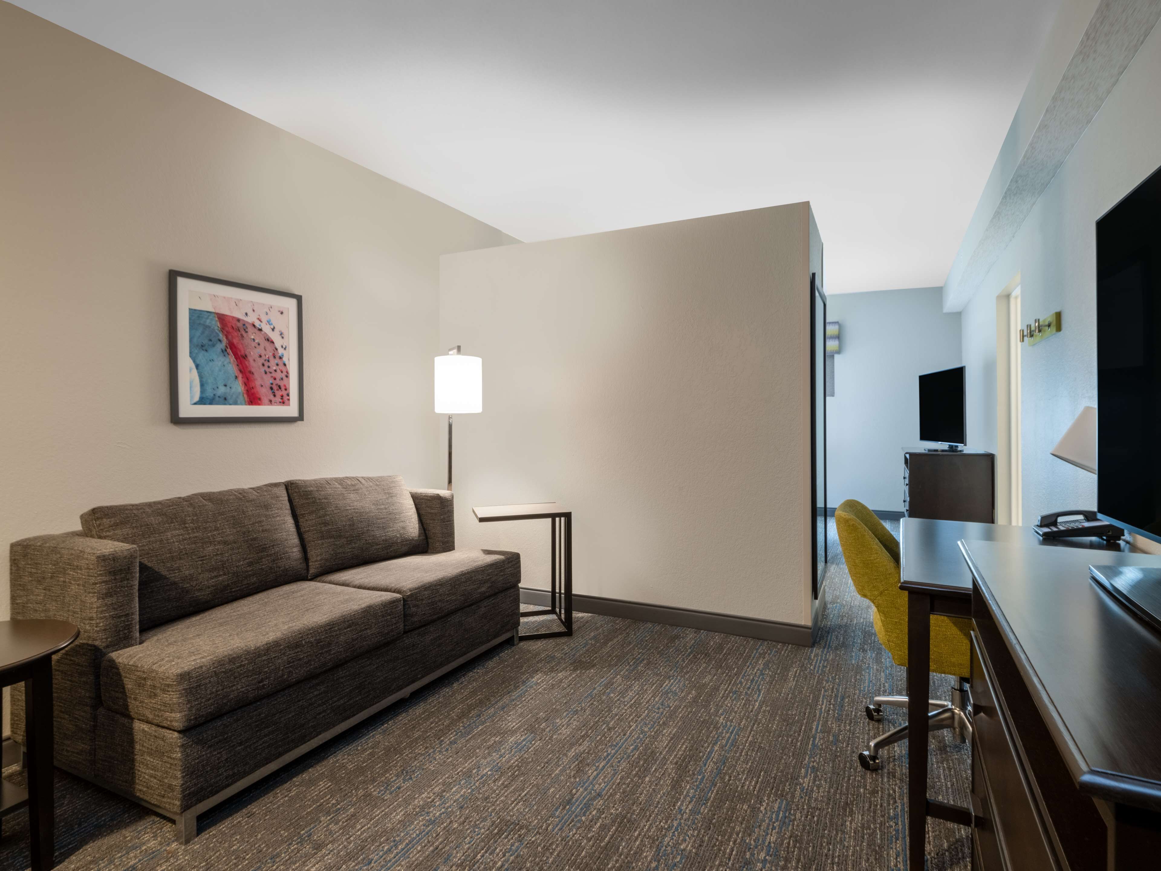 Una habitación de hotel con sofá, escritorio, silla, televisor y lámpara.