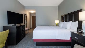 Habitación de hotel con cama, escritorio, silla, televisor y lámpara.