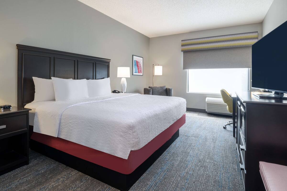 Een hotelkamer met een groot bed, nachtkastjes, een bureau met stoel, een televisie en een raam met uitzicht.
