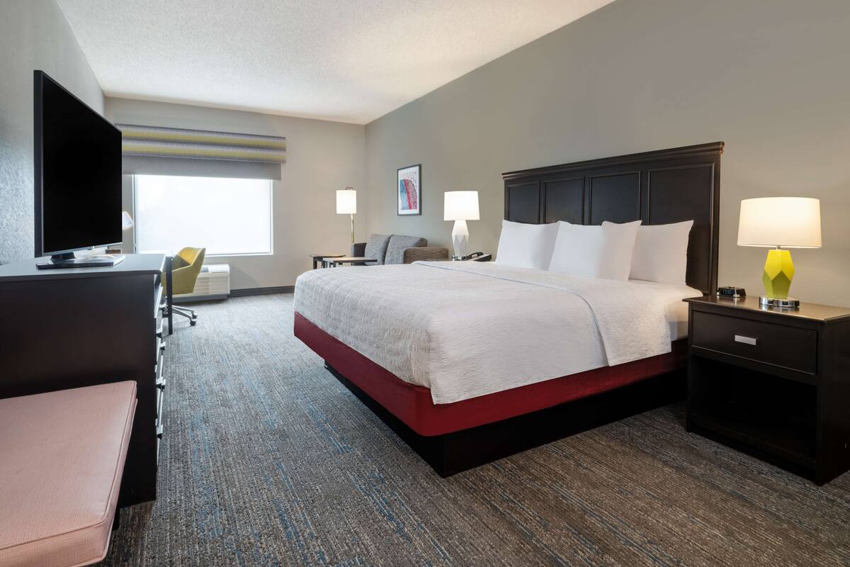 Een hotelkamer met een groot bed, een bureau met een computer, een stoel en twee bedlampjes.