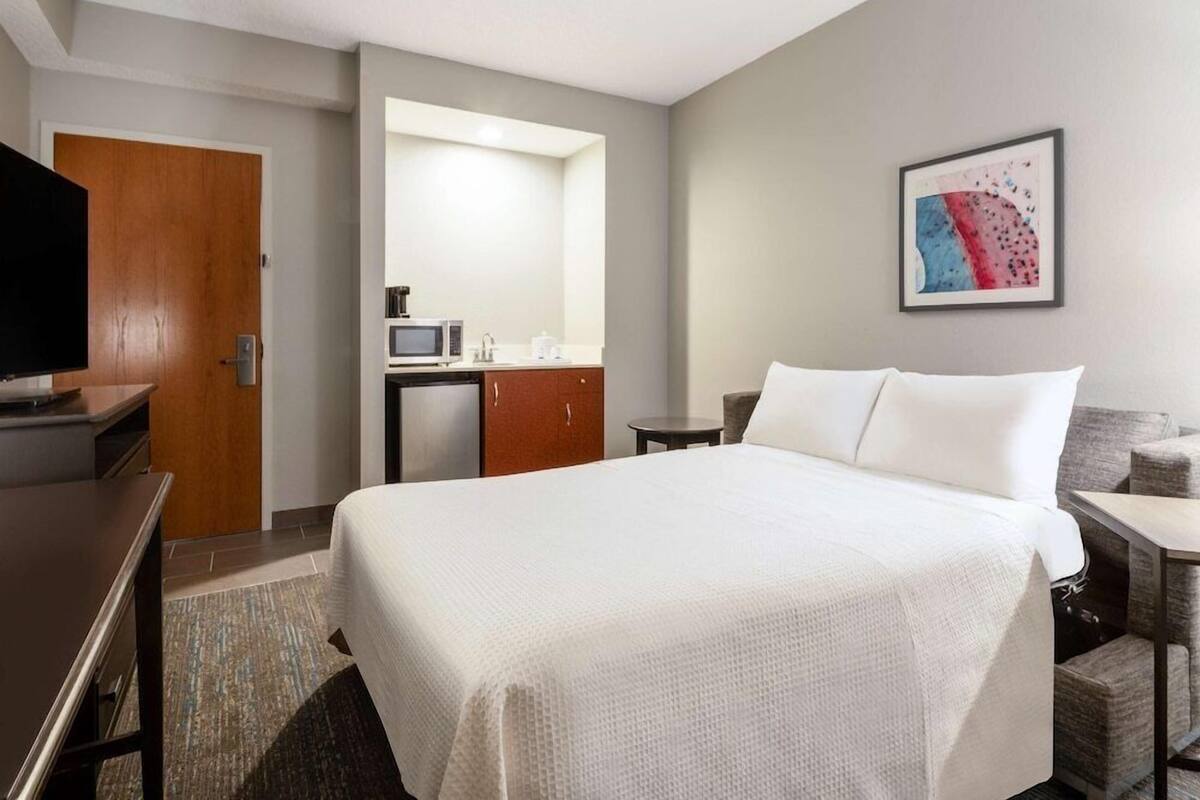 Een hotelkamer met een bed, een bureau, een televisie, een magnetron en een kleine kitchenette.