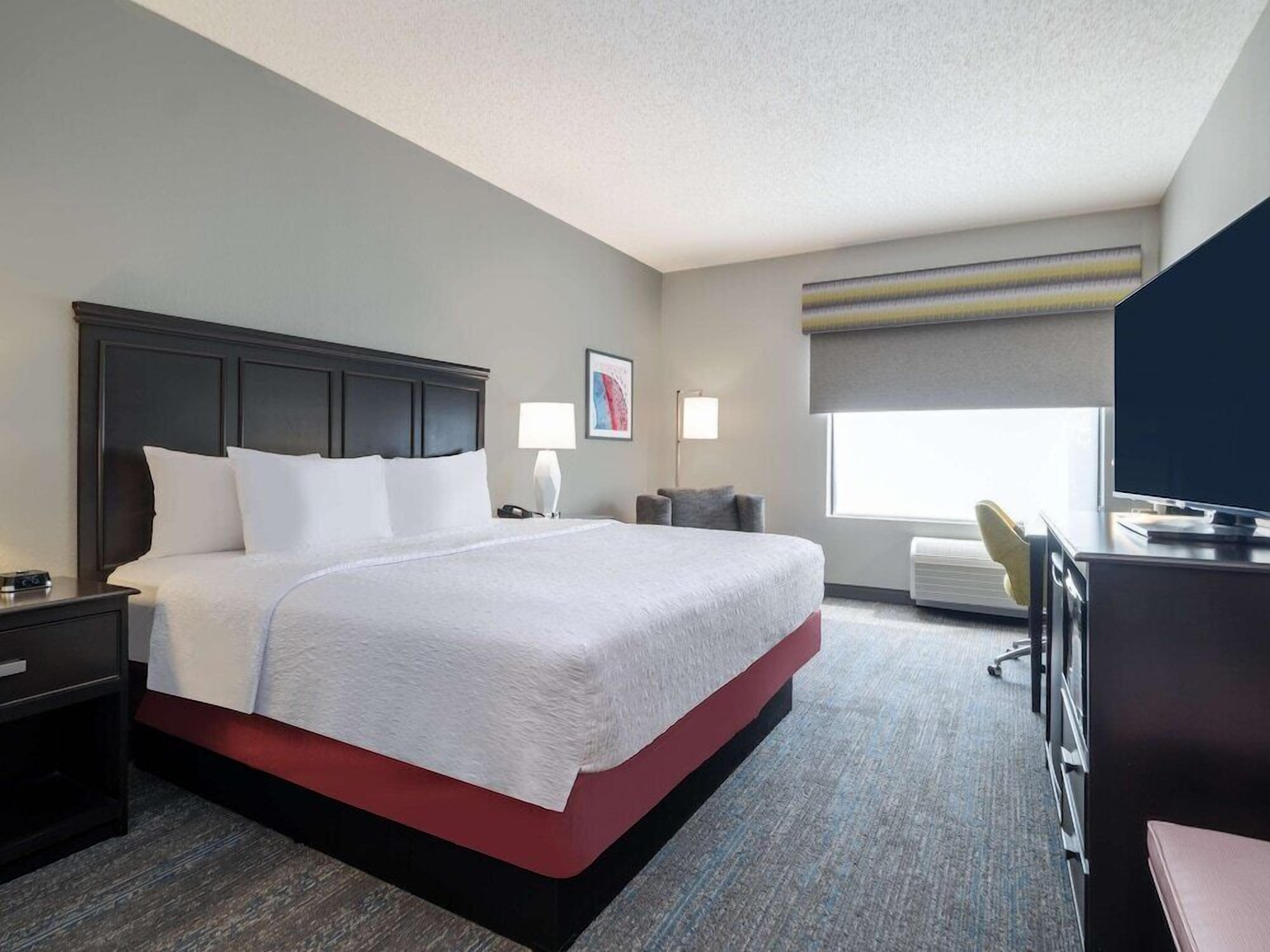 A hotel room with a large bed, bedside tables, a desk with a chair, a television, and a window with a view.