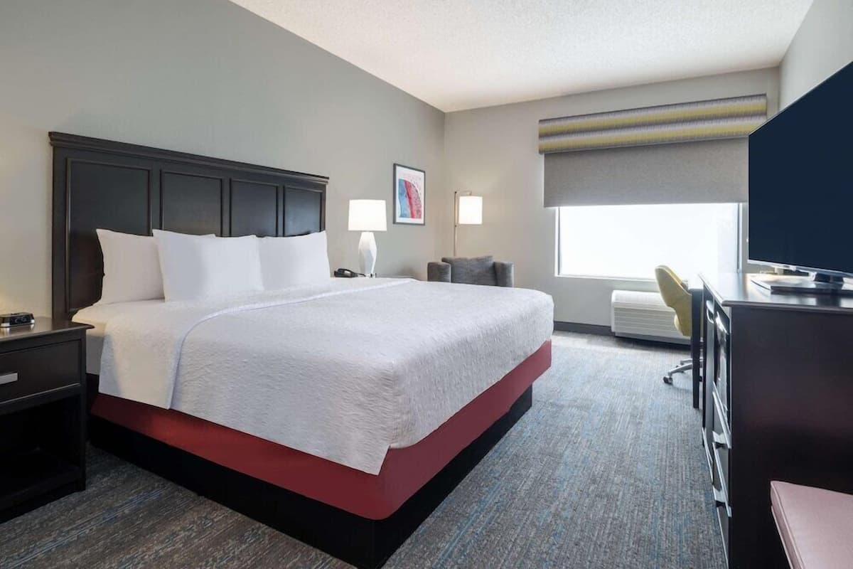 A hotel room with a large bed, bedside tables, a desk with a chair, a television, and a window with a view.