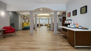 A hotel lobby with a reception desk, a red sofa, a yellow sofa, and a dining area with chairs and tables. - Hampton Inn West Palm Beach Florida Turnpike (West Palm Beach)