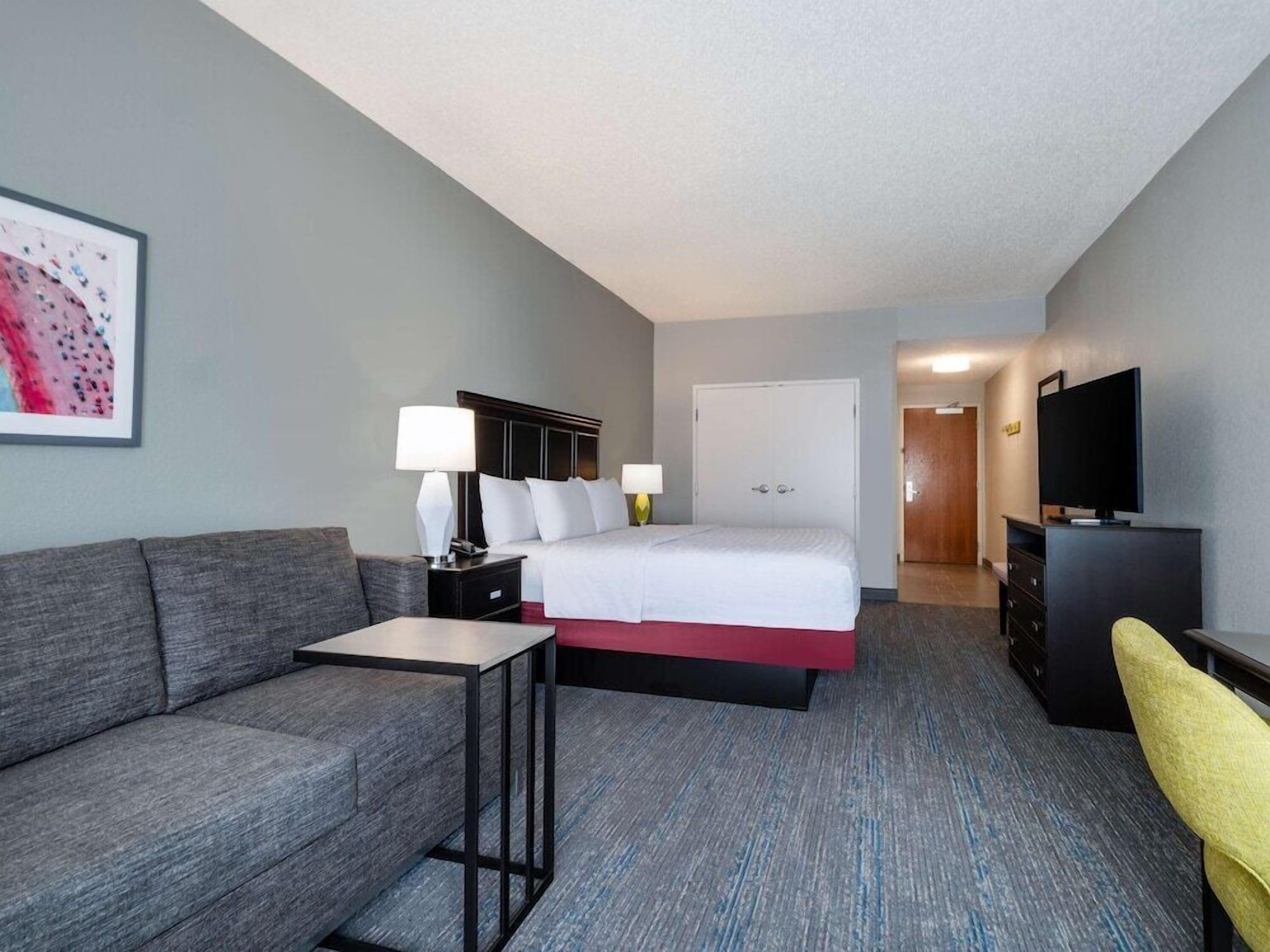 A hotel room with a bed, a desk, a chair, a TV, and a painting on the wall.