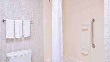 A bathroom with a toilet, three towels on a rack, a shower curtain, and a grab bar.
