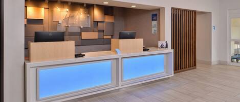 A reception desk with two computer monitors, a wooden panel wall, and a blue illuminated panel.