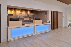 A reception desk with two computer monitors, a wooden panel wall, and a blue illuminated panel. - Holiday Inn Express Stockton Southeast by IHG (Stockton)