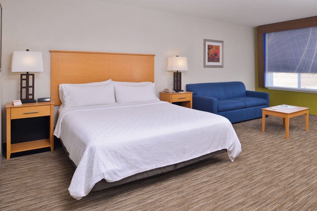 Una habitación de hotel con cama, dos mesitas de noche, una silla, una pequeña mesa y una ventana.