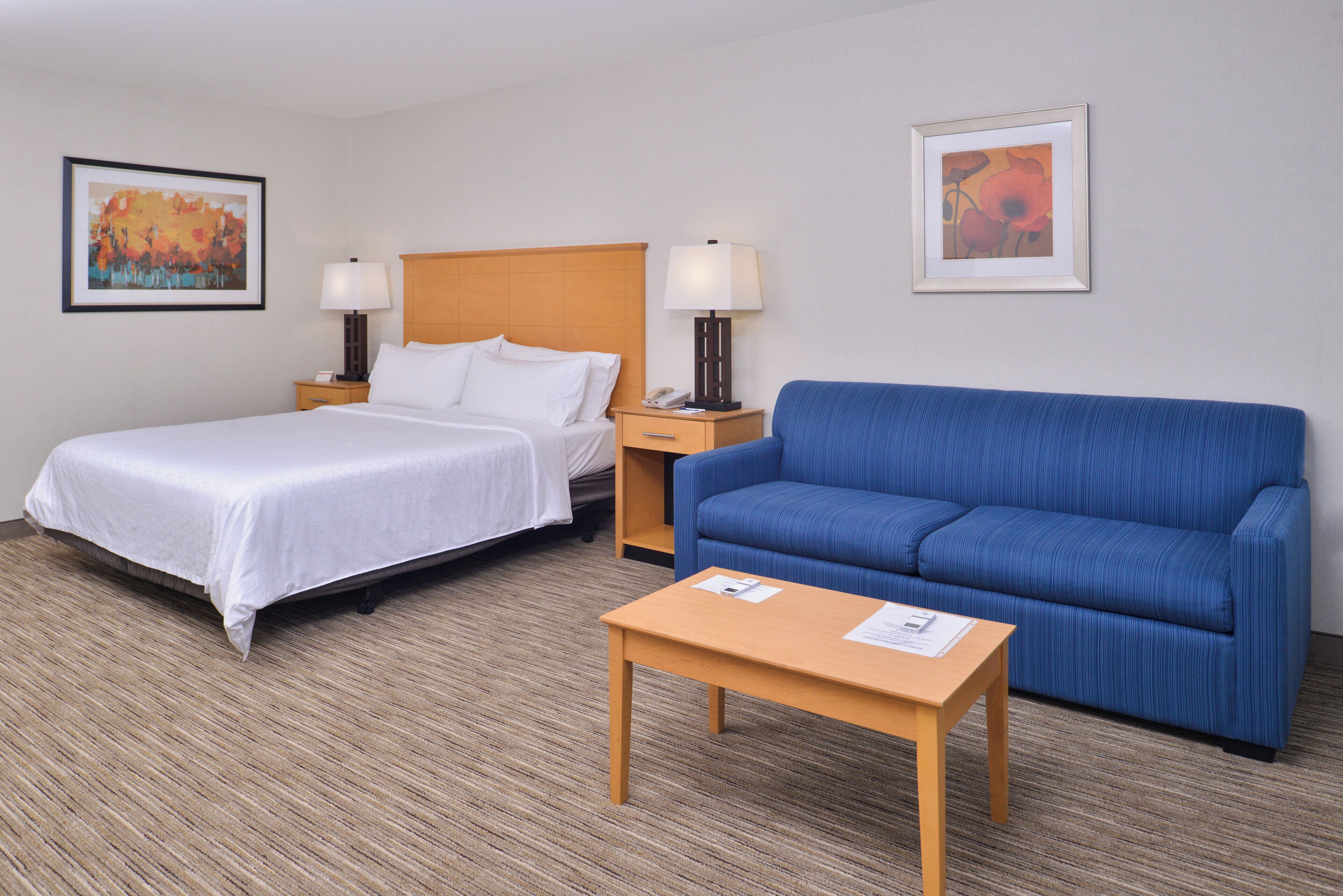 Una habitación de hotel con una cama, un sofá azul, una mesita de noche de madera y una pequeña mesa.