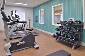 Un gimnasio con equipo cardiovascular, mancuernas y un espejo.