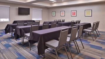 A conference room with tables and chairs, a projector screen, and framed artwork on the walls.
