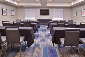 A conference room with rows of tables and chairs, a large screen at the front, and framed artwork on the walls. - Holiday Inn Express Stockton Southeast by IHG (Stockton)