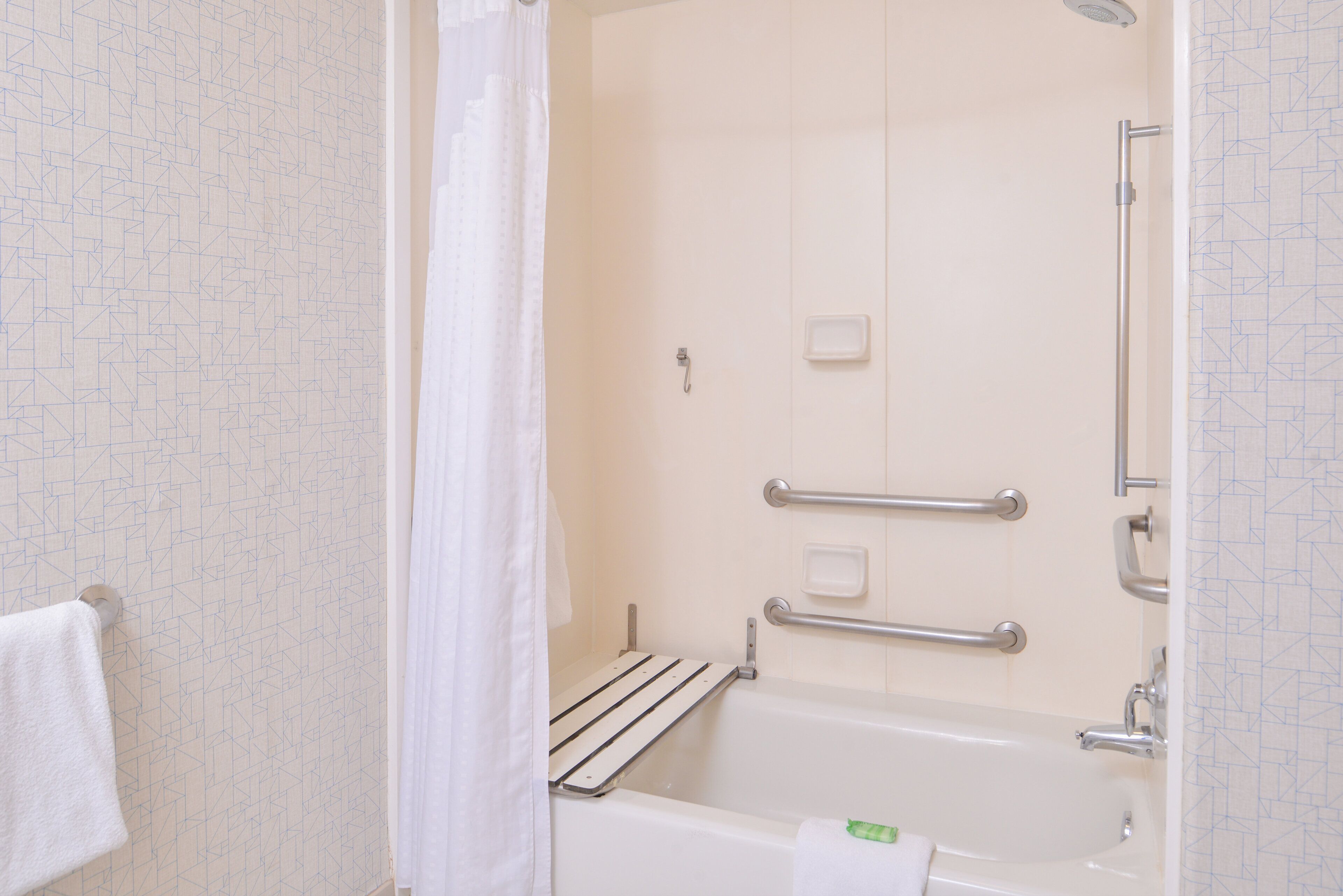 A bathroom with a bathtub, a shower curtain, a towel, and a handrail.