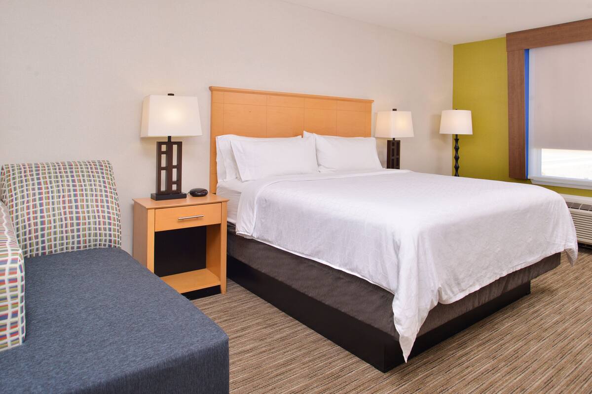 Une chambre d’hôtel avec un lit, des tables de chevet, une chaise et une fenêtre.