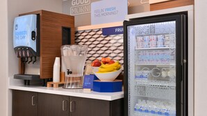 A breakfast bar with a beverage dispenser, a fruit bowl, and a refrigerated display of dairy products. - Holiday Inn Express Stockton Southeast by IHG (Stockton)