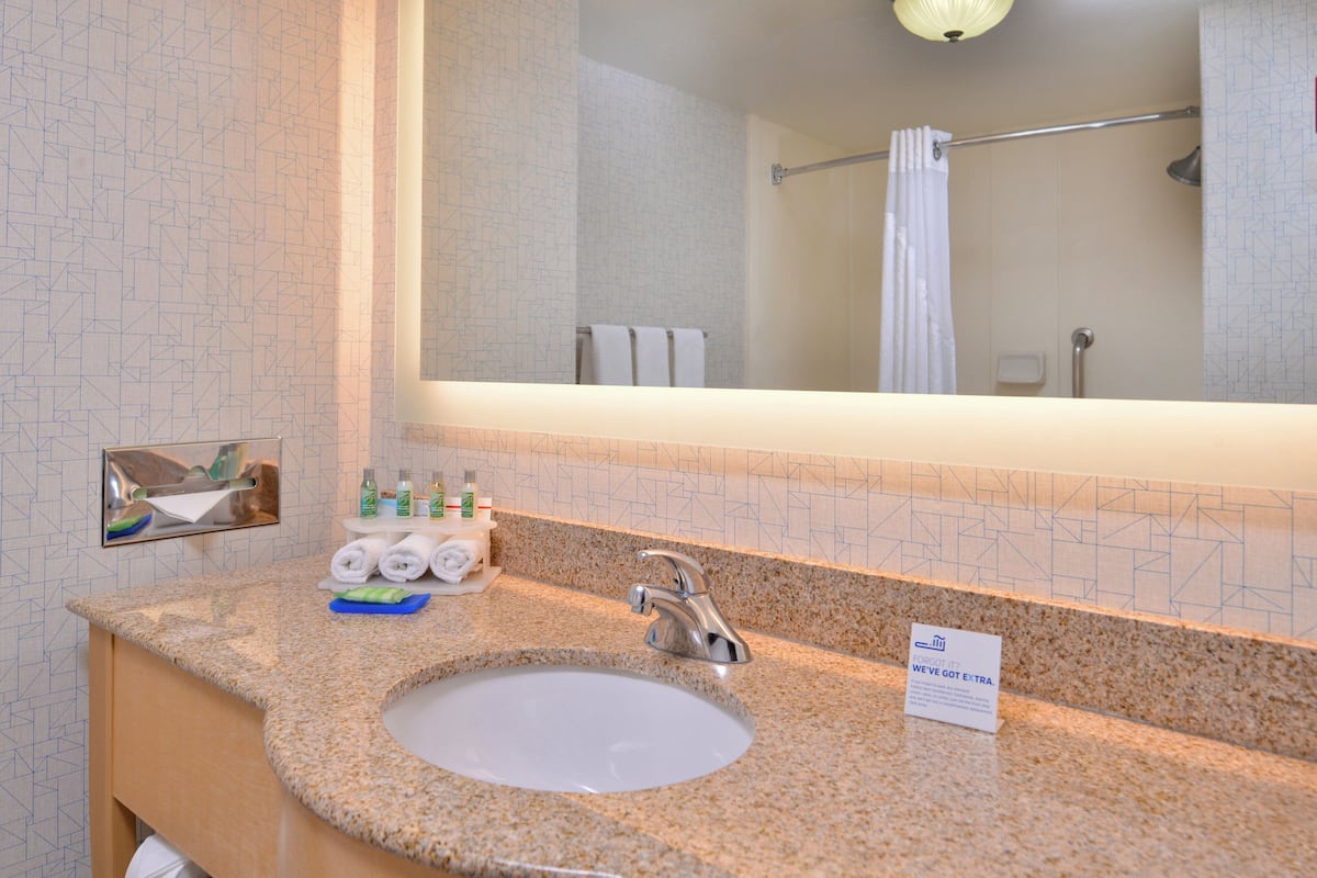 Une salle de bain avec un comptoir en granit, un lavabo, un miroir et un porte-serviettes.