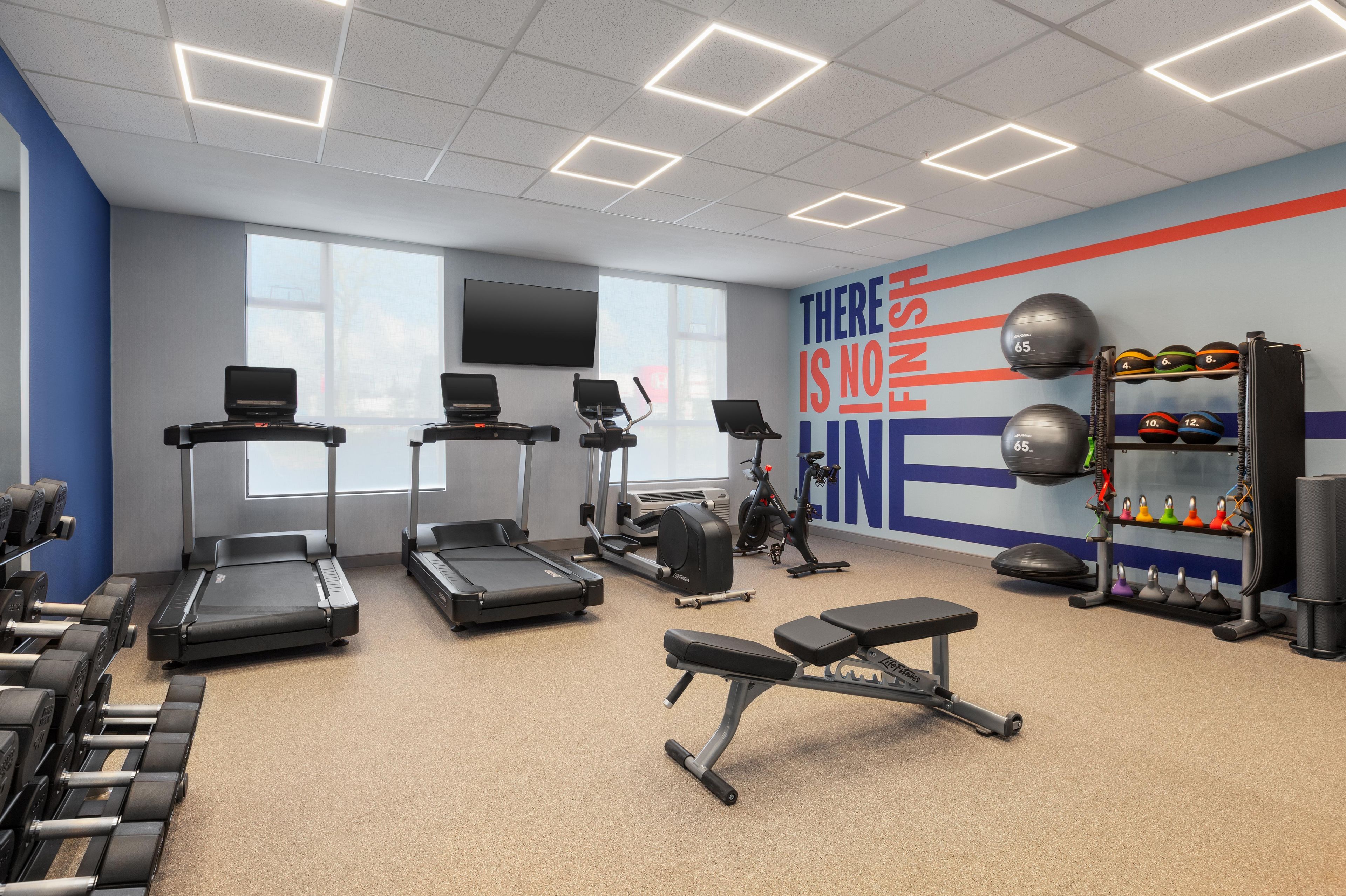 Ein Fitnessstudio mit Laufbändern, Gewichten und einer Wand mit motivierenden Sprüchen.