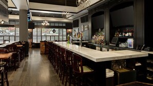 Zona de bar con una barra alargada, diversas opciones de asientos y un moderno candelabro.
