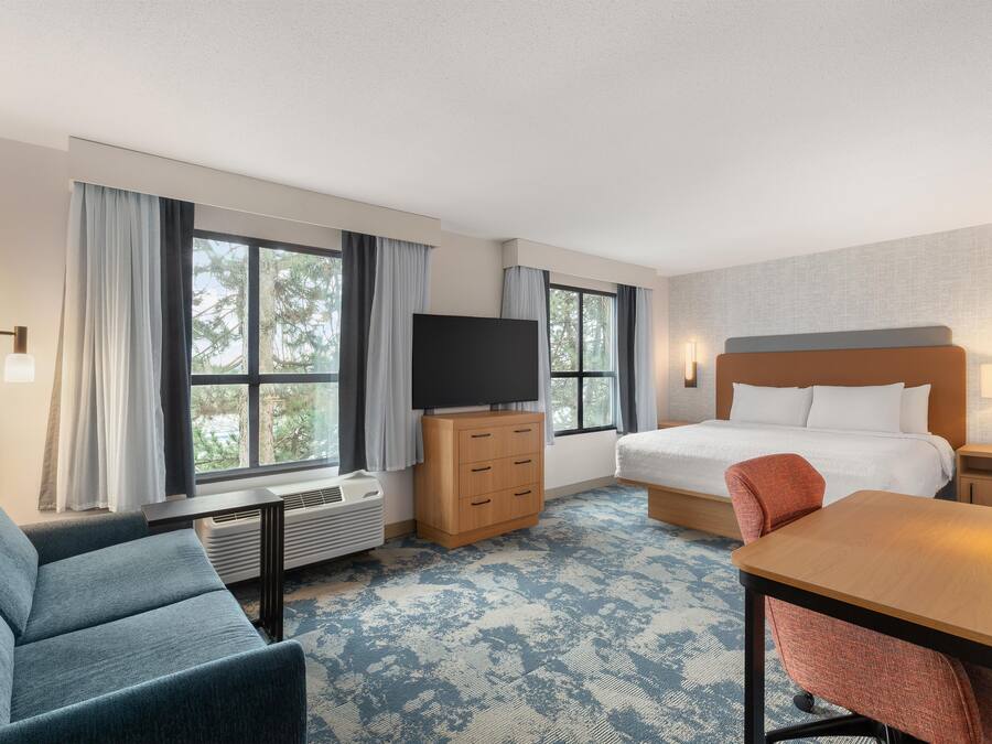 Una habitación de hotel con cama, televisión, escritorio, silla y ventana con cortinas.