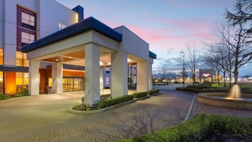 A modern building with a covered entrance, paved walkway, and landscaped area with a fountain.