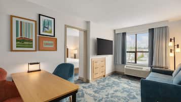 Habitación de hotel con cama, escritorio, silla, cómoda, televisor y una ventana grande con cortinas.