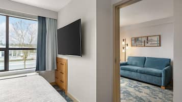Habitación de hotel con una cama, un televisor montado en la pared, un armario de madera, un sofá azul y una ventana con cortinas.
